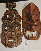 Two wooden masks side by side showing detailed carvings; left is Bakunawa sea dragon mask, right is Polynesian tiki mask