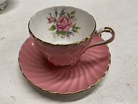 Front view of the pink teacup with floral rose pattern inside and gold rim and handle detail, set on matching saucer.