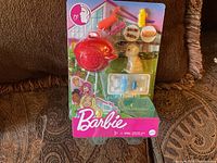 Front view of Barbie BBQ play set in sealed packaging showing red plastic grill, food pieces, dog figure, and accessories