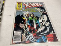Photo of the front cover of The Uncanny X-Men 210 comic book placed on a white surface in a plastic protective sleeve showing the artwork and text on the cover.