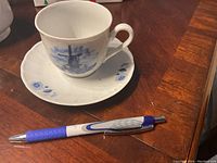 Teacup and saucer with blue windmill and floral design alongside pen for scale