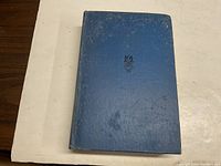 Front cover of the 1933 Modern Handbook For Girls, shows blue textured hardcover with black emblem.