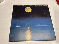 Front cover of Carlos Santana "Havana Moon" vinyl record sleeve showing full yellow moon over water with boats and harbor in the distance.