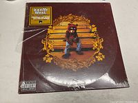 Front cover of unopened vinyl record with Kanye West bear mascot on bench and album title sticker