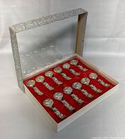 Closed original decorative case with transparent lid showing the 12 white metal dragon chopstick holders inside on red lining.