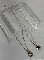 Two silver necklaces displayed with pendants, showing chain length and pendant design.