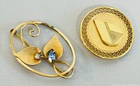 Oval brooch front showing leaf design and two small gemstones, gold finish, minor wear visible
