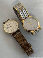 Two wrist watches side by side on a neutral surface, showing front faces and bands.