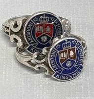 Close-up of two sterling silver Kingsmill class rings showing enamel crests and ornate silver bands.