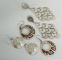 Three pairs of silver earrings displayed flat showing front design including chandelier, colorful geometric, and tree of life styles.