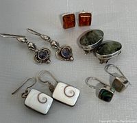 Five pairs of silver earrings arranged on fabric background, showing variety of stones and styles.