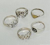 Five silver rings displayed on a light surface, showing designs including elephant, dolphins or fish, pentagram, open hearts, and plain band.