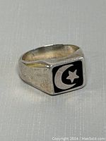 Close-up front angle showing the crescent and star symbol on black background of the ring face, silver band showing minor wear.