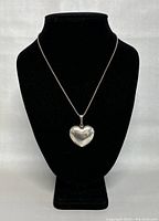 Front view of the sterling silver heart pendant necklace displayed on black stand showing shiny, reflective heart pendant.