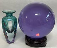 Hand blown art glass vase next to purple crystal ball on wooden stand, showing colors and scale