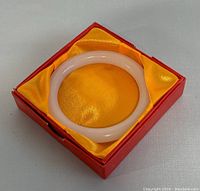 White natural jade bangle shown in red box lined with yellow satin fabric.