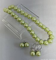 Photo of the green pearl necklace, a pair of matching green pearl earrings, all with round green pearls.