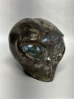 Front and angled views of a polished hematite alien skull sculpture with flashing blue labradorite eyes.