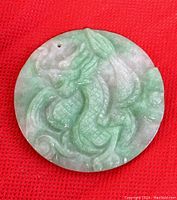 Front side of round green and white jade pendant carved with a detailed dragon motif.