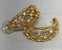 Semi hoop 14k gold earrings with lattice design and clear rhinestones, shown from side angle highlighting curvature and rhinestone detail.