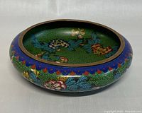 Side angled view showing the colorful floral cloisonne decoration with green background and cobalt blue rim.