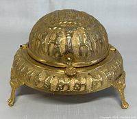 Front view of vintage gold-tone roll top caviar dish server with embossed animal designs and ornate feet.