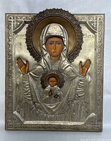 Front view of metal oklad icon depicting the Virgin Mary with raised arms and infant Christ on chest