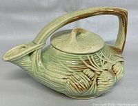 Front and side view of green glazed vintage ceramic teapot with pine cone and needle embossed design, showing handle, spout and lid.