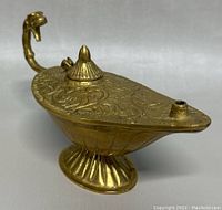 Full view of vintage solid brass Aladdin oil lamp showing engraved lid, dragon handle, and fluted base.