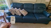 Blue leather couch with throw pillows, displayed in a living room with window lighting. Measuring 84" x 39" x 32" noted by seller. Shows some creases and mild wear.
