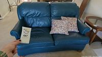Blue leather loveseat with two patterned throw pillows on seat, showing full front view.