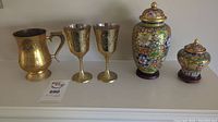 Overall view of the brass decorative pieces including mug, two goblets, and two covered jars with colorful cloisonné designs.