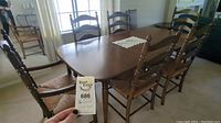 Solid wood dining table with six matching ladder back chairs around it inside a room. Table has smooth finish with rounded edges.
