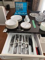 Wide view of porcelain dinnerware, gravy bowl, and utensil drawer showing flatware assortment.