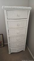 Front view of white wicker 6-drawer tall dresser showing curved drawer fronts and woven wicker texture