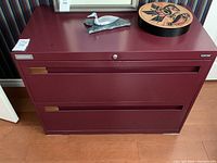 Front view of red steel filing cabinet closed, showing three drawers and top surface with decorative items.
