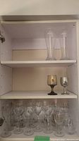 Shelf with two tall clear beer glasses on top, one amber goblet and one light gray goblet on middle shelf, and multiple clear stemmed wine glasses on bottom shelf.