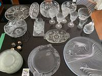 Overview of various clear glassware and salt shakers on black table surface showing multiple etched plates, bowls, goblets, and metal salt shakers.