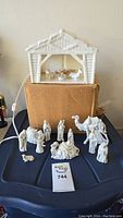 Full view of the nativity set with the shelter elevated on a box and all ceramic figures arranged in front, showing the white ceramic with corded light shelter on top and various figurines below including animals and human figures.