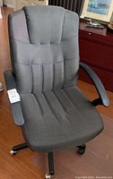 Photo of grey fabric office chair with armrests and wheels on hardwood floor