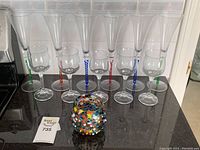 Seven clear stemware and aperitif glasses with twisted colored stems in green, red, and blue arranged on a counter.