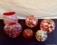 Full lot view showing two 7-inch vases (heart-shaped multicolor and candy cane red and white), two 5-inch red globes with colorful millefiori, 3-inch red paperweight, and 4-inch hanging multi-colored orb.