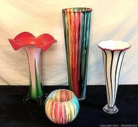 Four colorful art glass pieces displayed side by side on black surface with white backdrop, showing size and color details