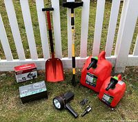 Photo showing all items including jump starter box, snow shovel, brush/scraper, two gas containers, spotlight, emergency shovel, tire inflator box, and cables.