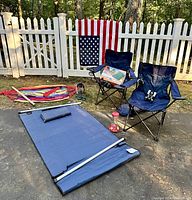 View of entire outdoor birding setup including two folding camp chairs, hammock, swinging cloth seat, inflatable camp mattress, American flag, binoculars on chair, and bird feeders