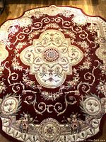 Top down view of the full Chinese wool rug laid on the floor showing scarlet field and cream border with floral medallion.