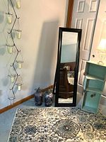 Photo of rug with coordinating decor items including a tall dark wood frame mirror, robin's egg blue wooden boxes, two decorative jars, and a candle holder vine on the wall.