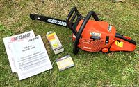 Echo CS-310 chainsaw laid out on grass with instruction manual, safety manual, and a new packaged chain visible.