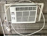Front view of the GE window air conditioner with power cord coiled around and accordion side panels extended.