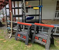Full lot showing two sawhorses, extension ladder on the ground, and long-handled tools leaning on shelving units.